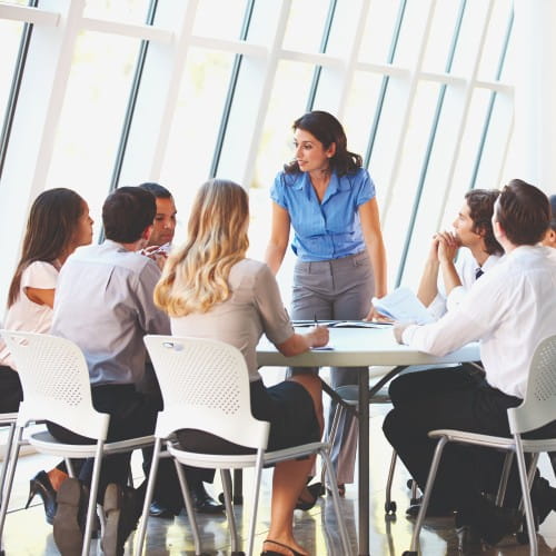 Büro-Mitarbeitende sitzen um einen runden Tisch - Eine Frau präsentiert