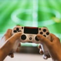 Hände halten Spielkonsole vor einen großen Bildschirm